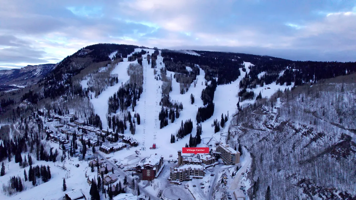 A vibrant winter scene featuring the snow-covered slopes of Purgatory Resort, with the Village Center nestled at the base. Ski lifts are visible in the background, surrounded by frosted trees, capturing the heart of the ski-in/ski-out experience and the lively atmosphere of the resort village.