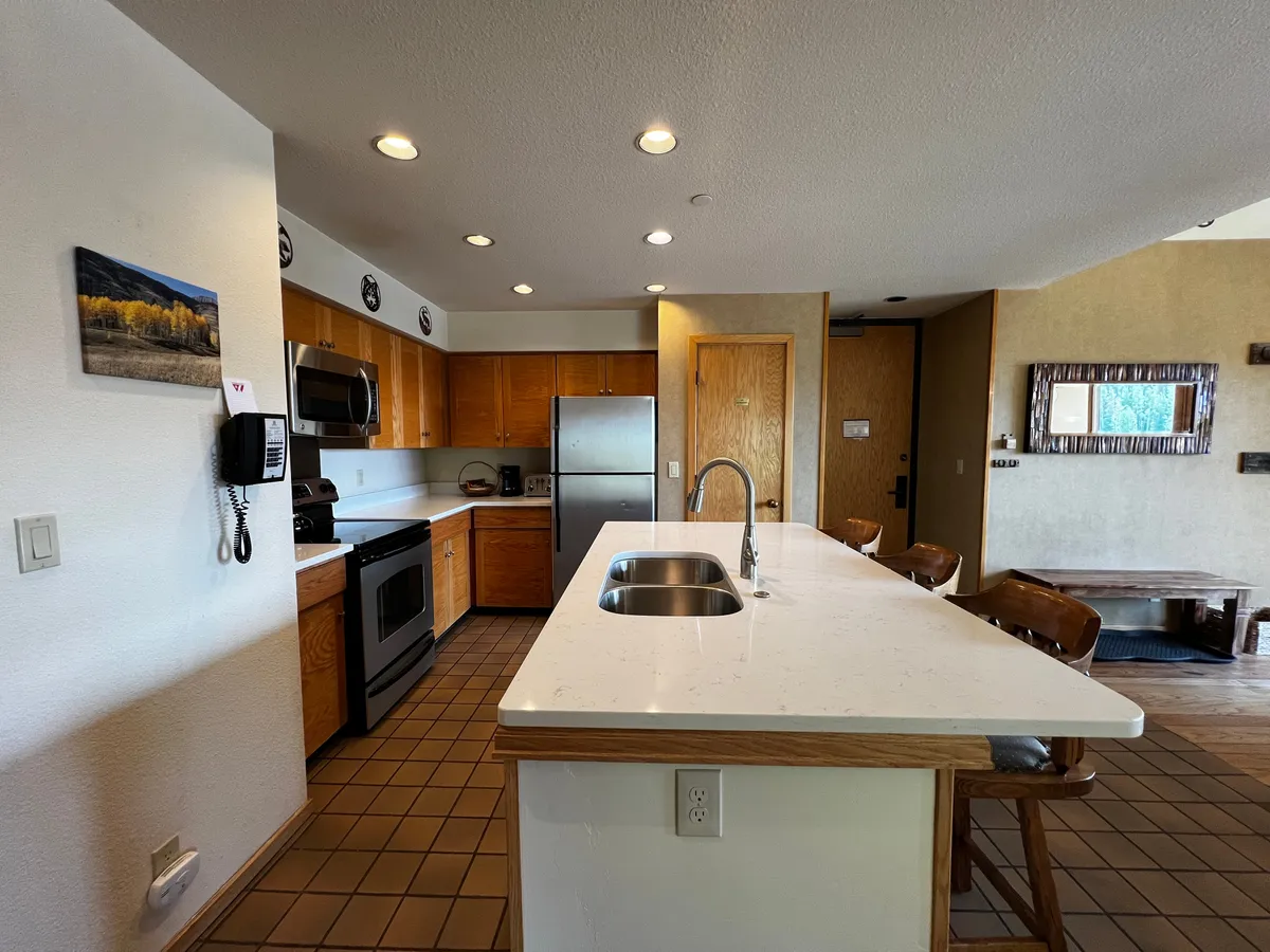 This image features an inviting kitchen space with a prominent kitchen island, stainless steel appliances, wood cabinets, and tasteful wall art. The layout is open, allowing easy movement between cooking and socializing zones, and the lighting creates a warm, welcoming atmosphere ideal for gatherings.