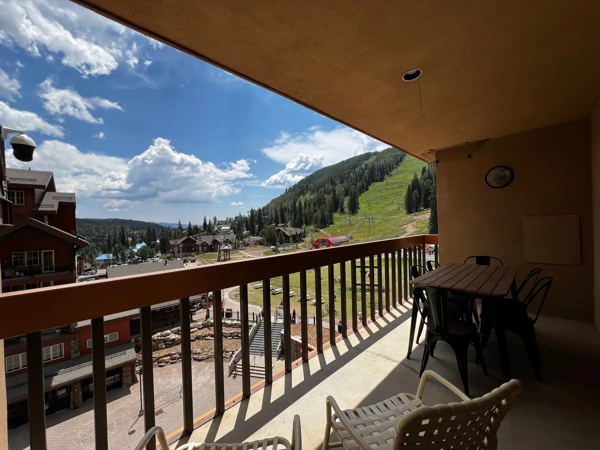 A tranquil balcony space with comfortable seating overlooks the mountains and adjacent buildings. The scene suggests opportunities for outdoor dining, socializing, relaxing after a day on the slopes, or watching the sunset together as a group or family.